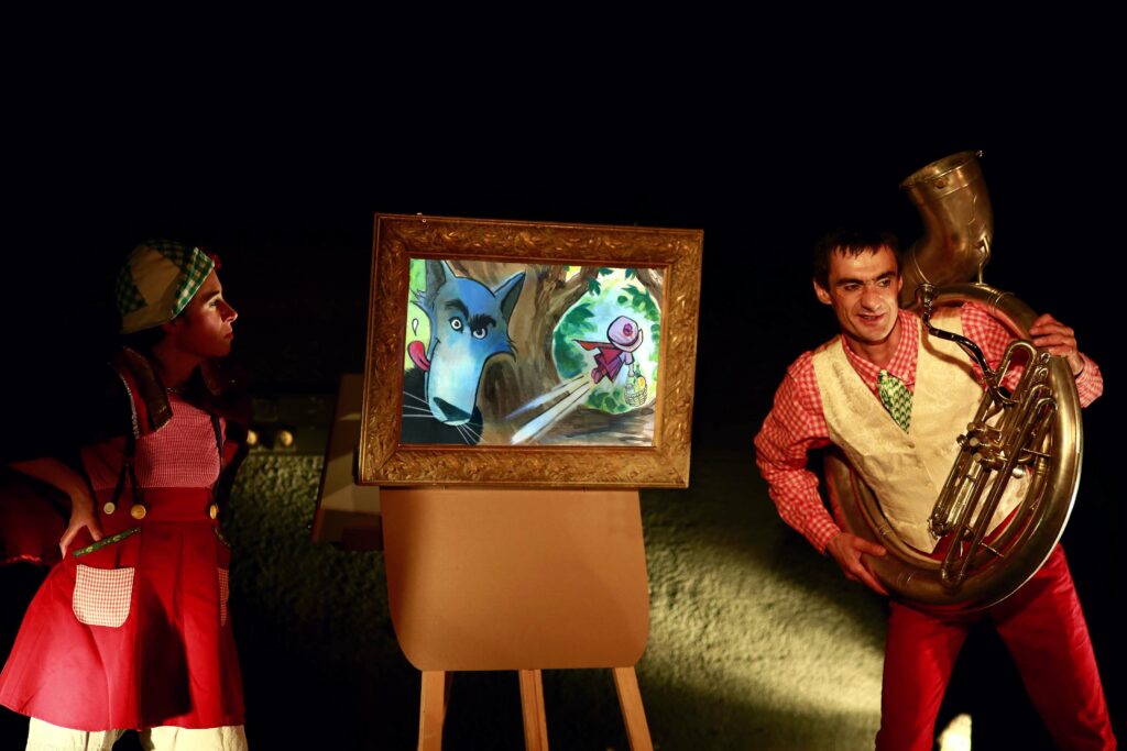 Deux comédiens en jeu avec un hélicon, et un kamishibaï qui illustre le petit chaperon rouge